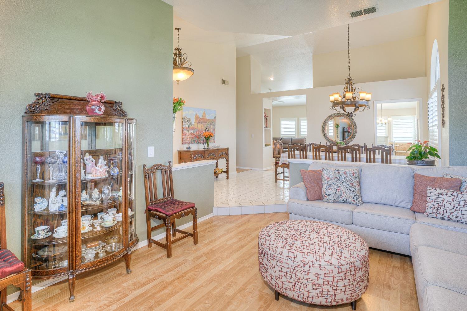 Open-plan living and dining room with a pale sectional, patterned ottoman, and wooden display cabinet.