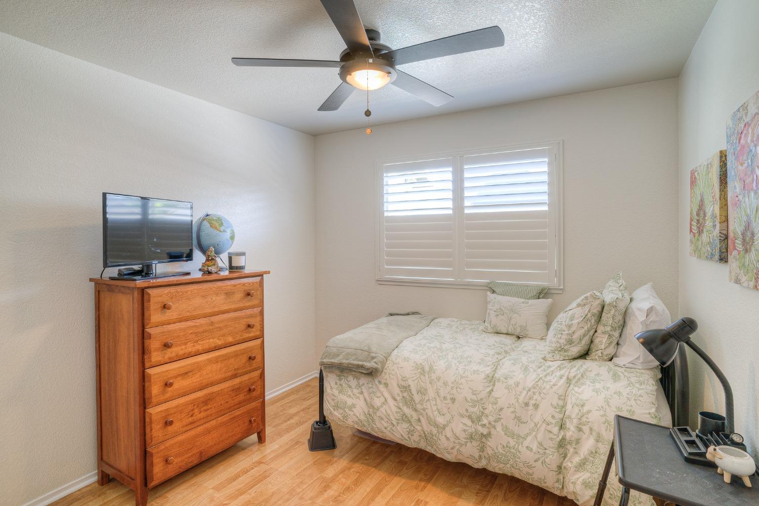 Bedroom with a floral bed, white plantation shutters, and a wooden chest of drawers.