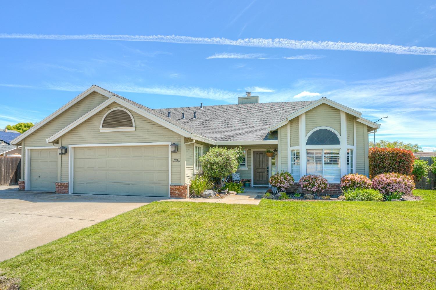 Single-story beige home with a two-car garage, arched windows, and flowering front landscaping.