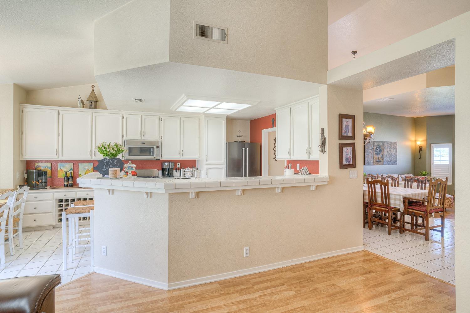 Kitchen with white cabinets and tiled breakfast bar opening into a dining room.