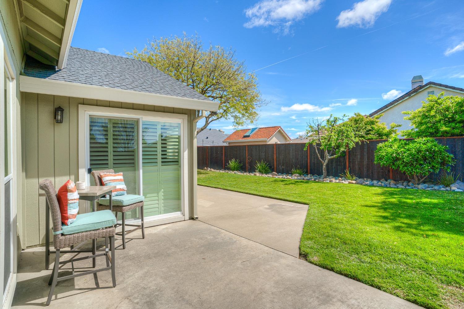 Backyard patio with wicker seating beside a lawn and fenced garden.
