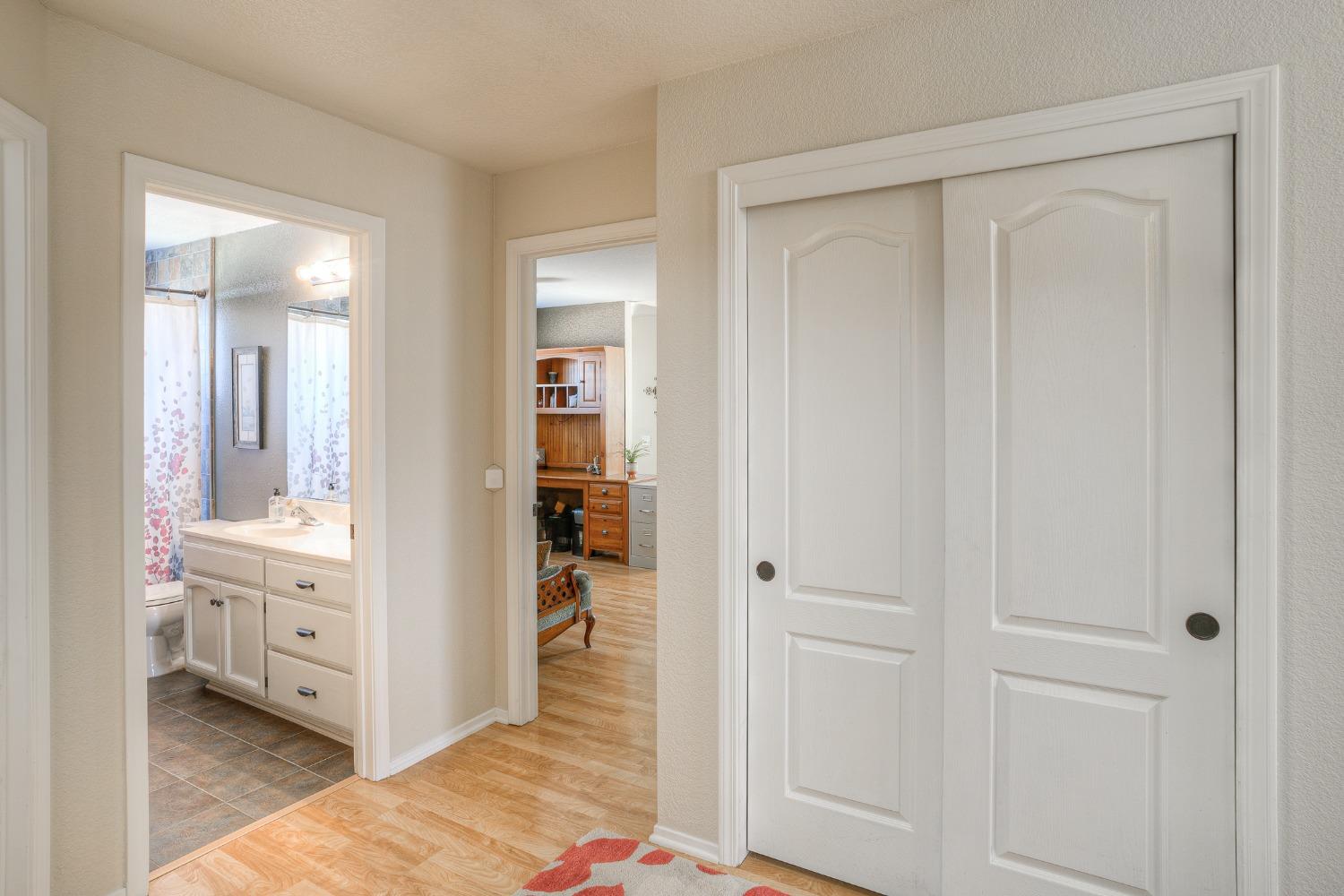 Hallway with white sliding closet doors, opening to a bathroom and a room with wood cabinetry.