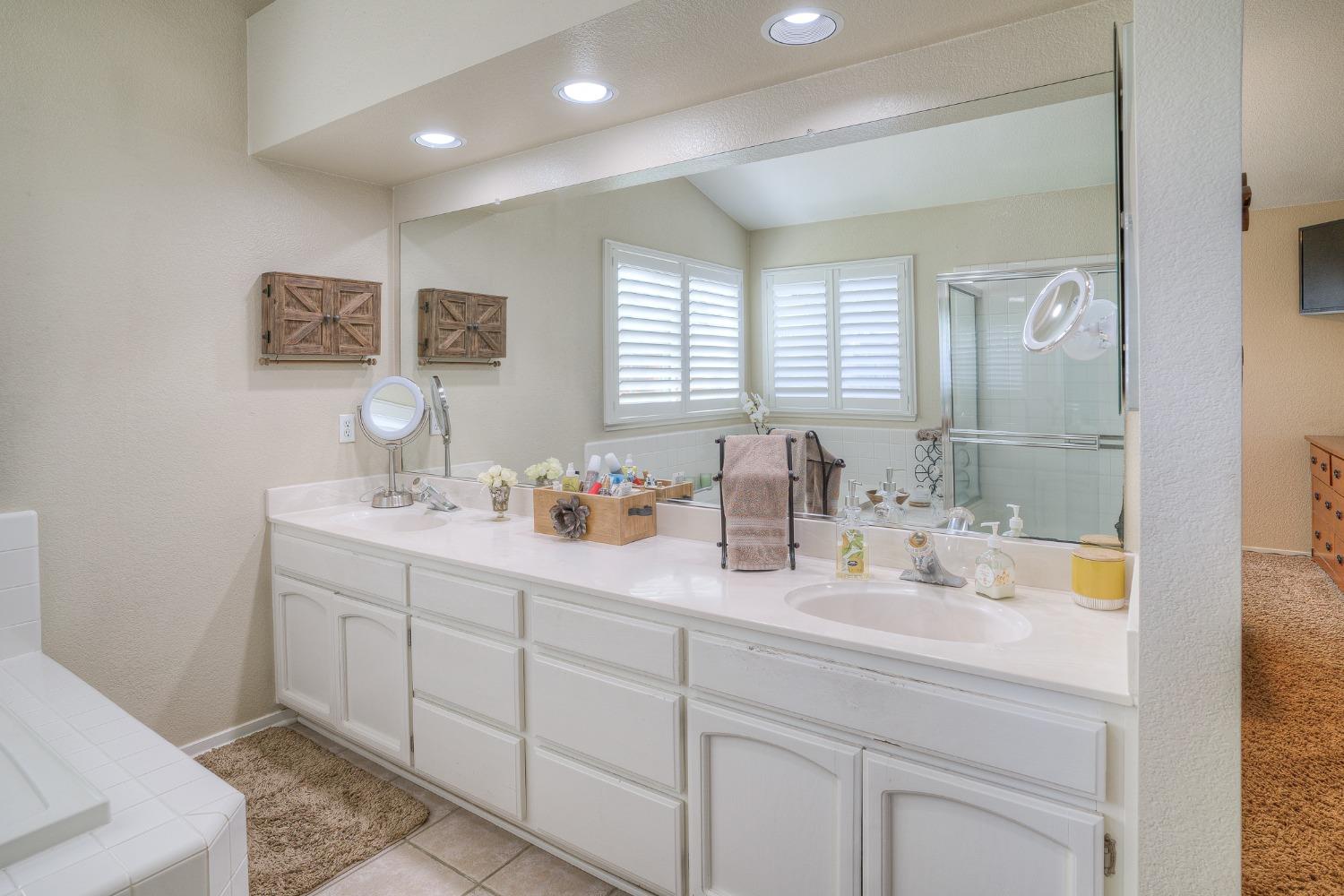 Bathroom with a long double-sink vanity, mirrored wall, shuttered windows, and glass-enclosed shower.