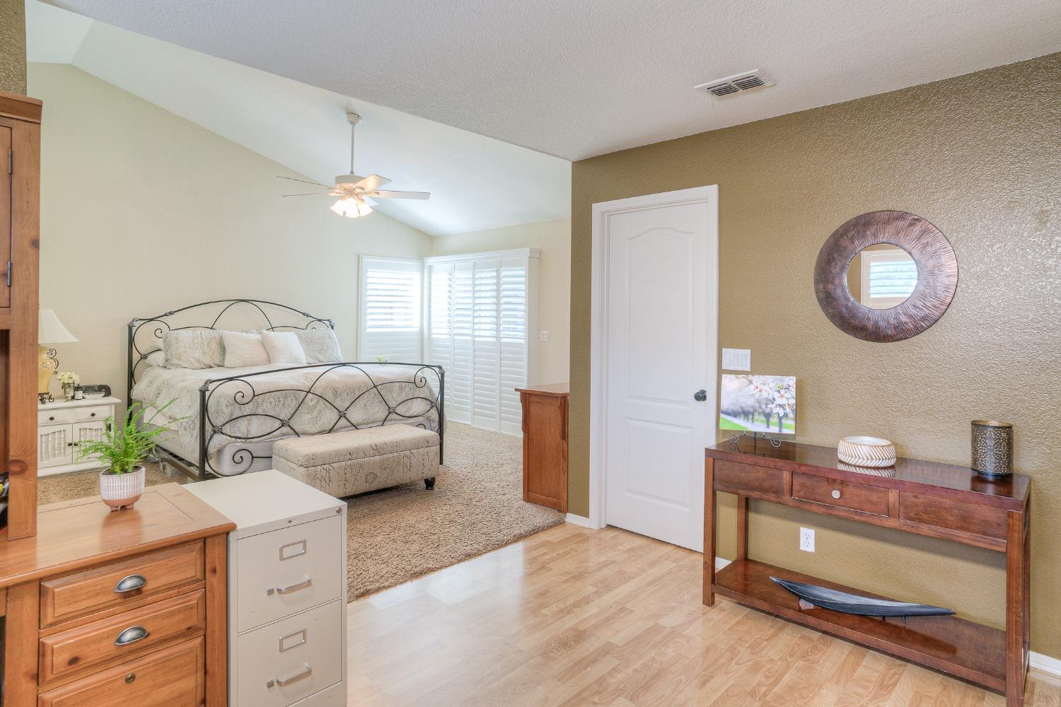 Furnished bedroom with a black metal bed and plantation shutters beside a wood-floored entry.