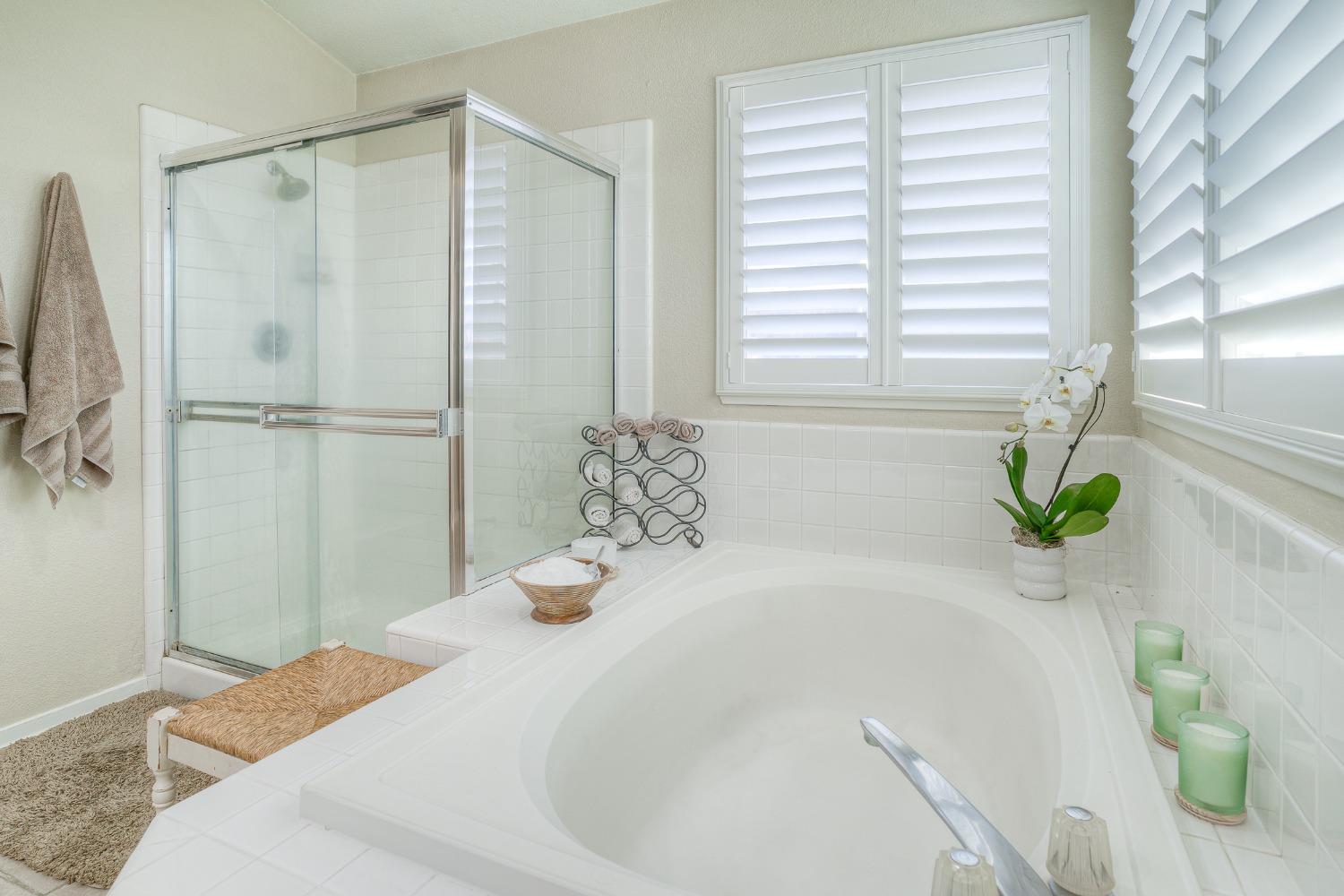 Bathroom with a large soaking tub, glass-enclosed shower, and plantation shutters.