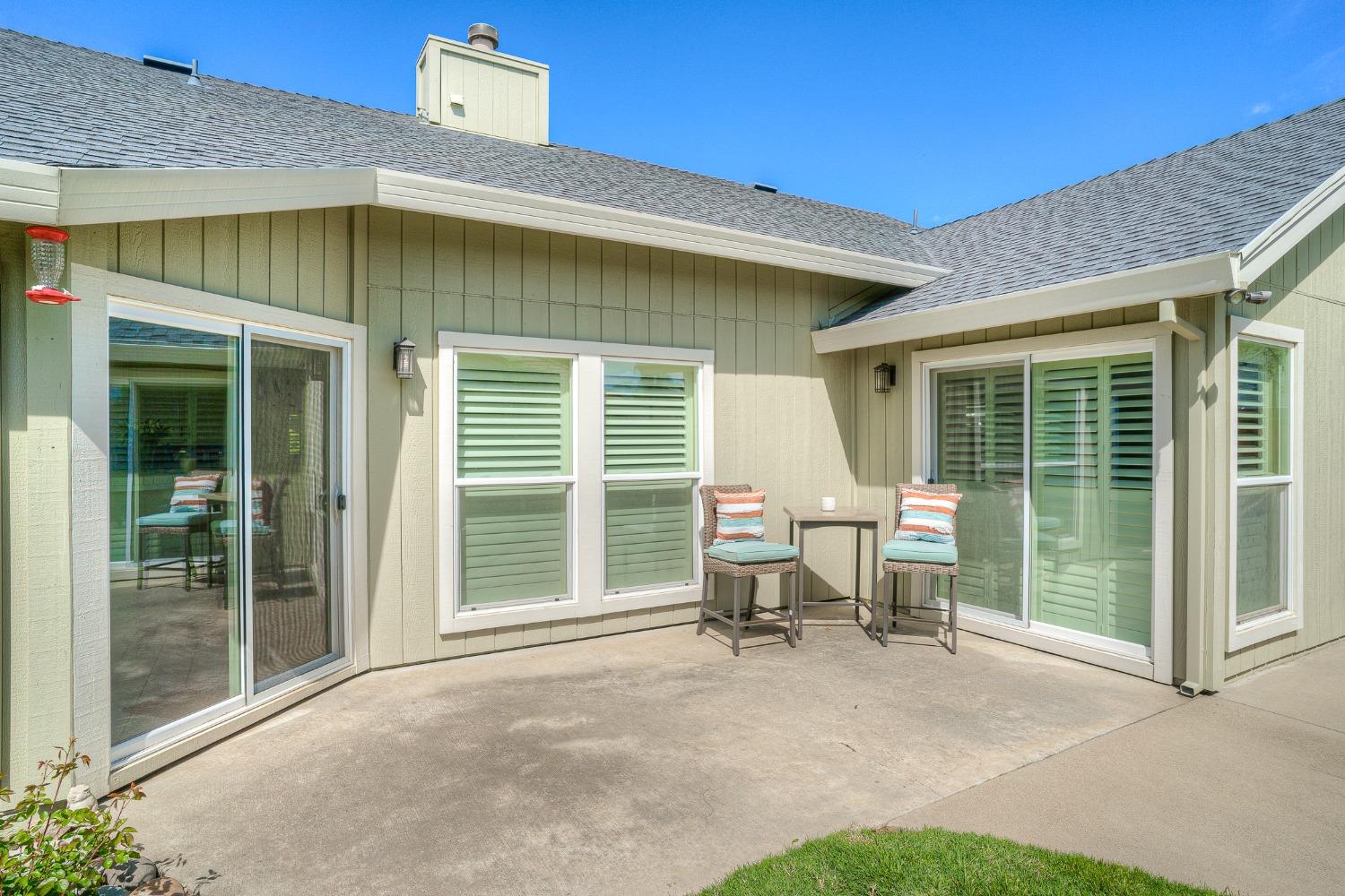 Home patio with sliding glass doors, shuttered windows, and two chairs beside a small table.