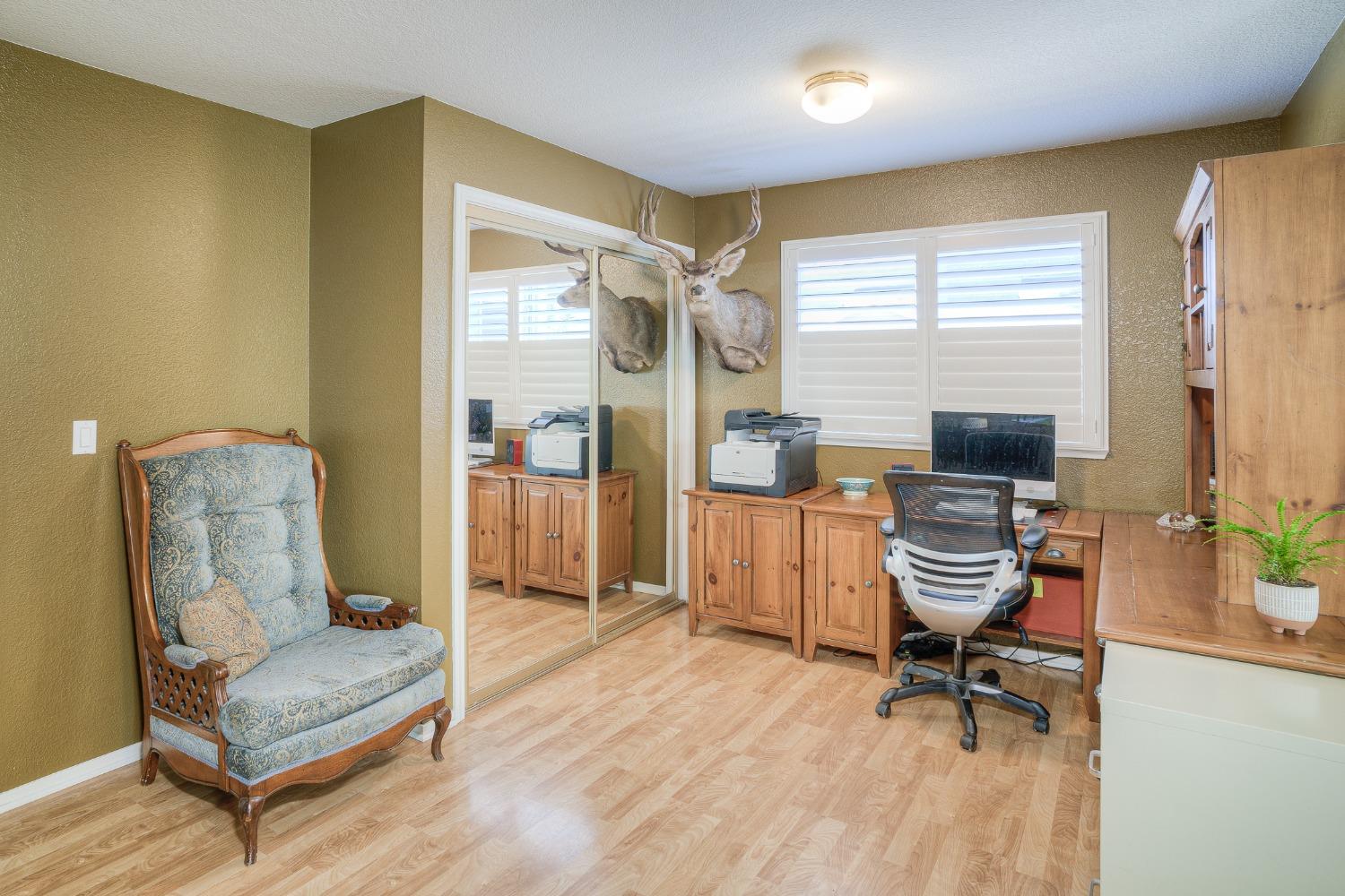 Home office with wooden desk and cabinets, mirrored closet doors, and a patterned armchair.