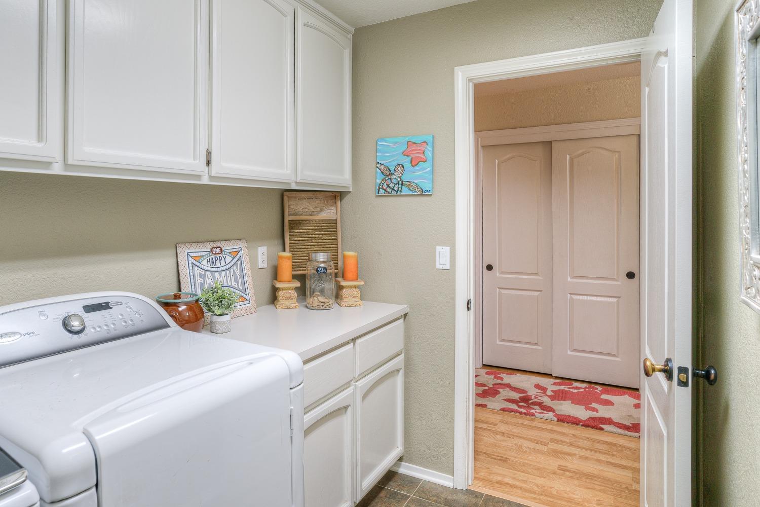Laundry room with white appliances, overhead cabinets, and a counter leading to a hall with double doors.