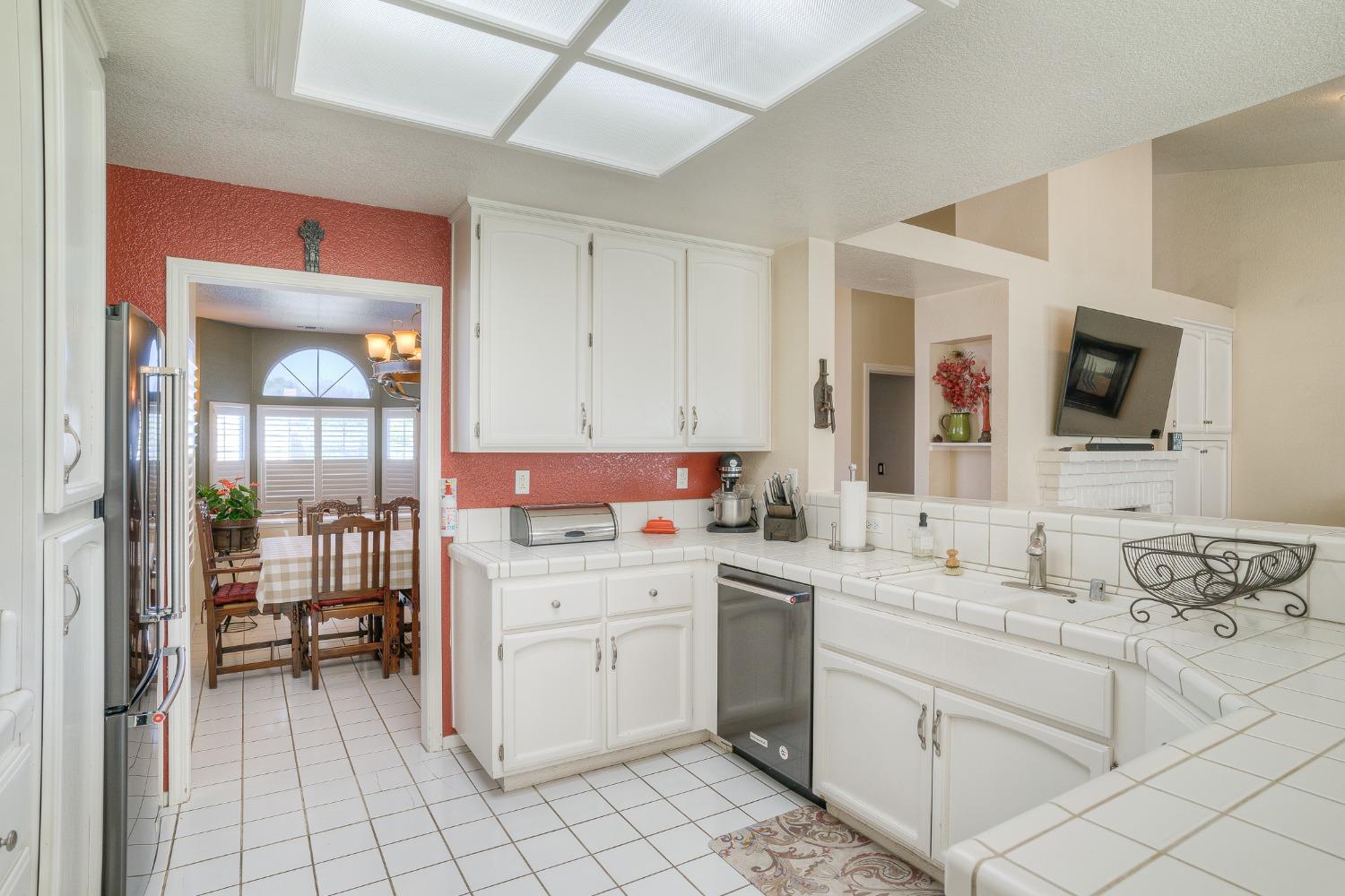 Kitchen with white cabinets and tiled counters, opening onto a dining room with a table and chairs.