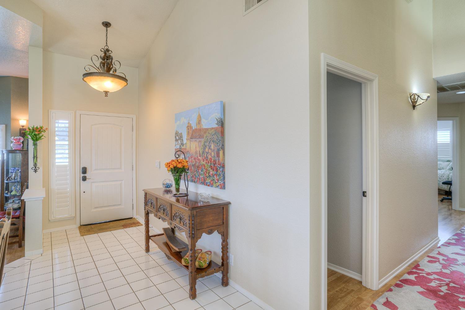 Entry foyer with white tile flooring, a carved wood console table, and colorful floral artwork.