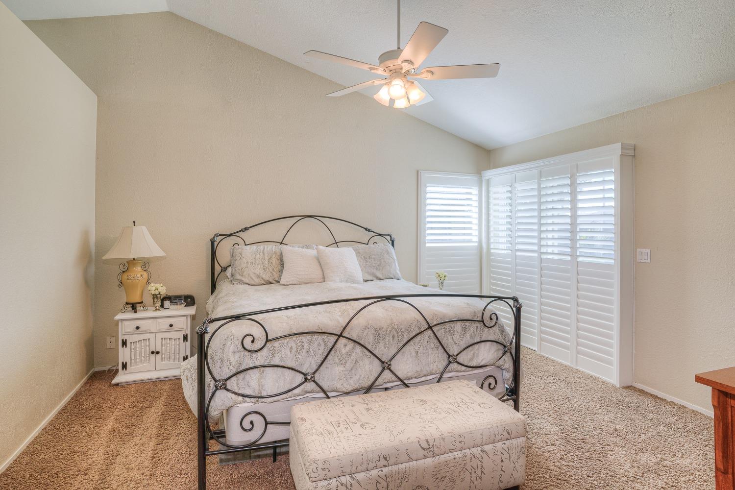 Bedroom with a metal bed frame, patterned bedding, vaulted ceiling, and plantation shutters.