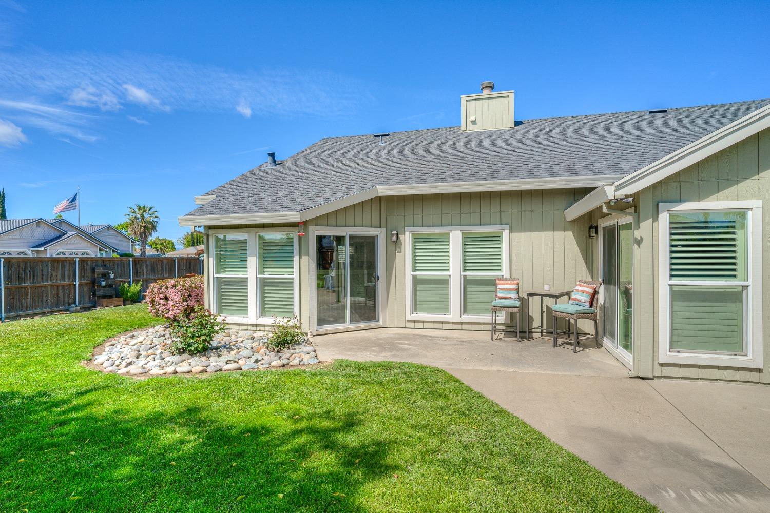 Rear patio with two chairs and table beside the home, overlooking a broad lawn and landscaped garden.