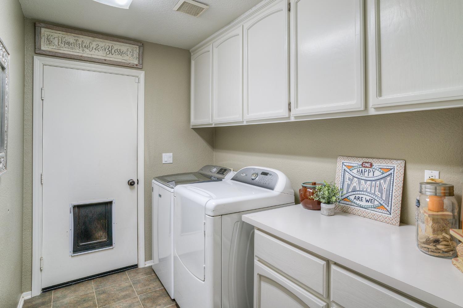 Laundry room with white washer and dryer, upper cabinets, countertop, and a pet flap in the door.