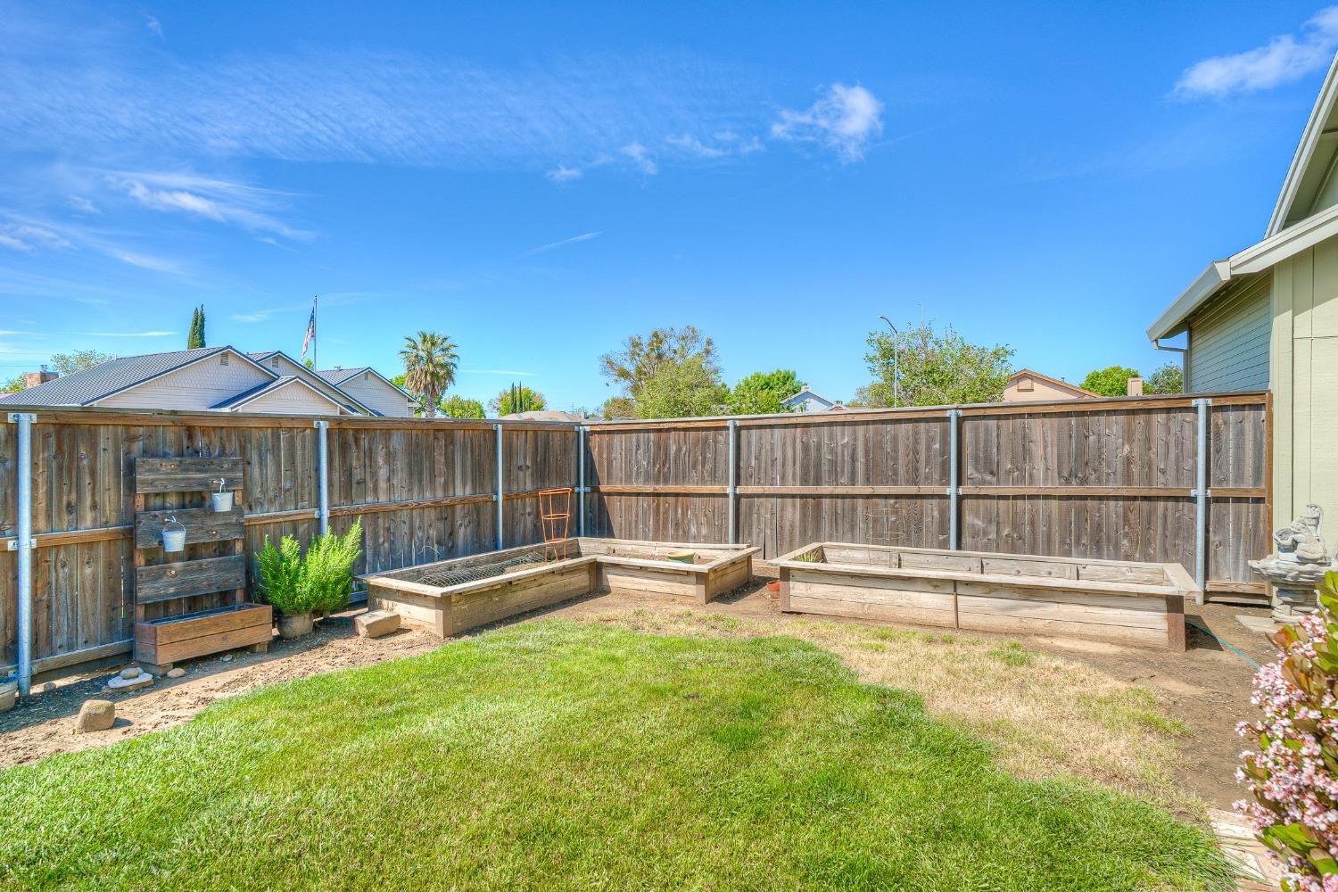 Fenced backyard with a lawn and raised wooden garden beds.