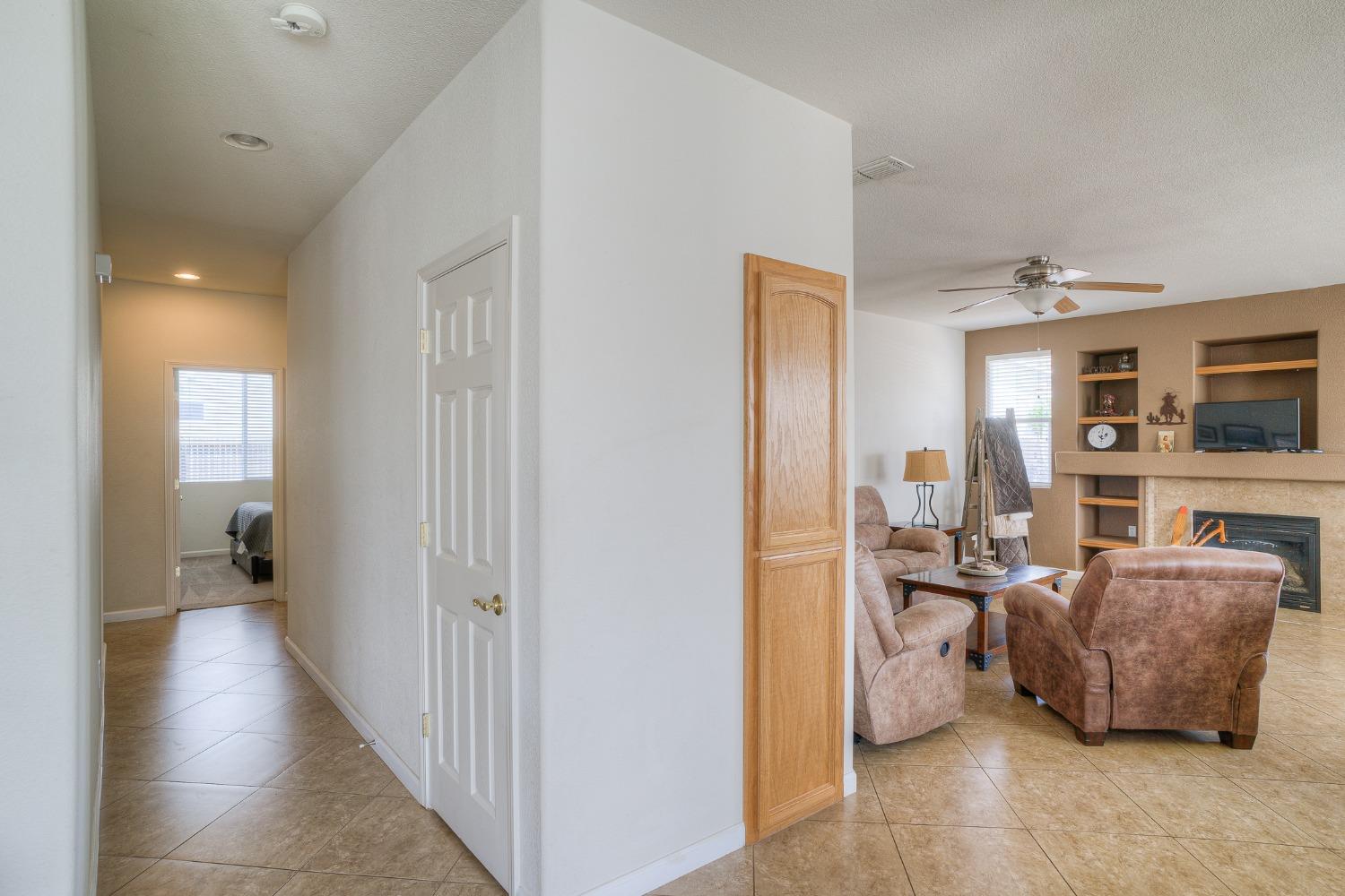 Living room with a fireplace, built-in shelves, and tan recliners beside a tiled hallway.