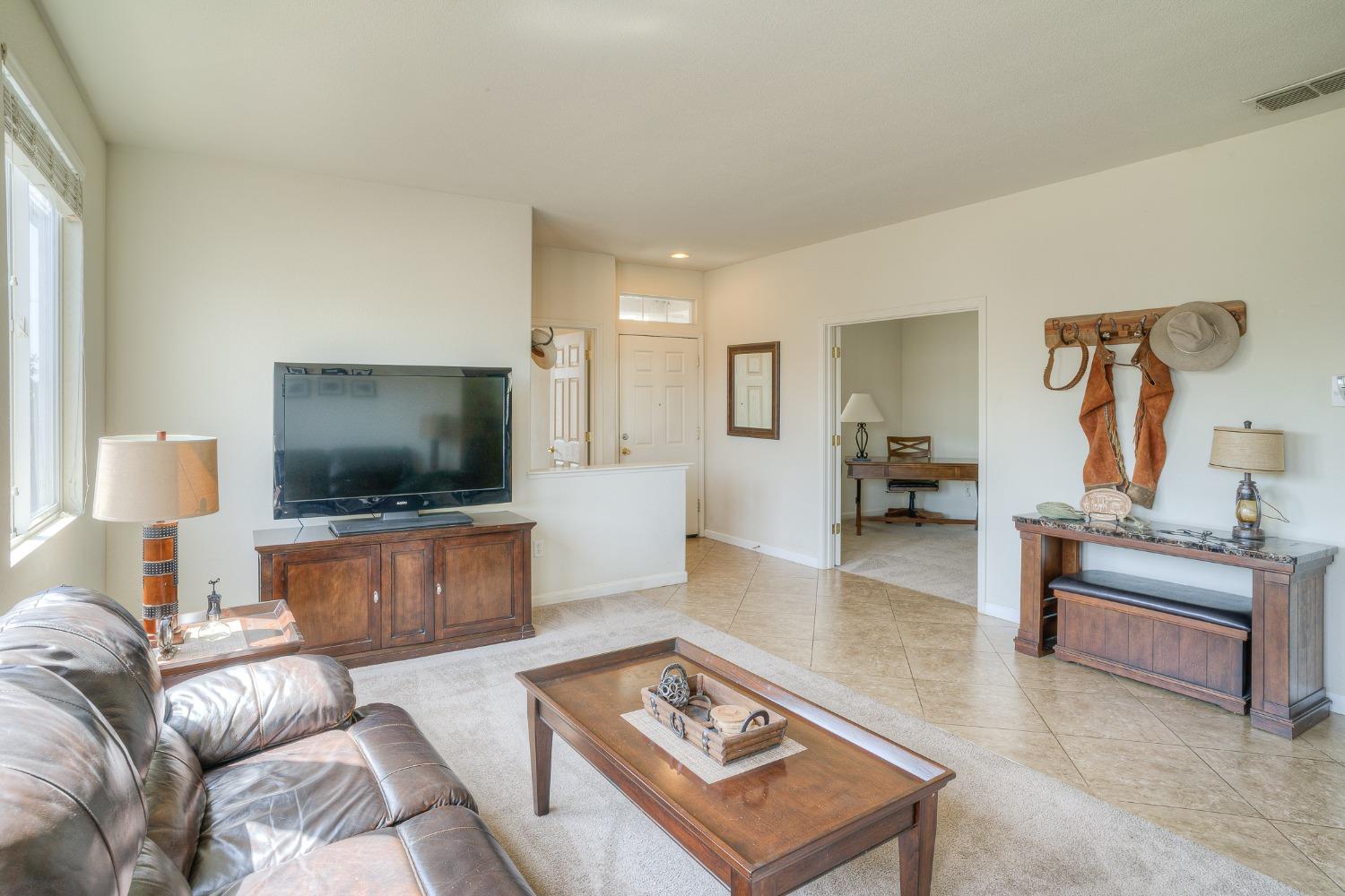 Living room with a leather sofa, wooden coffee table, and TV cabinet beside an open office doorway.