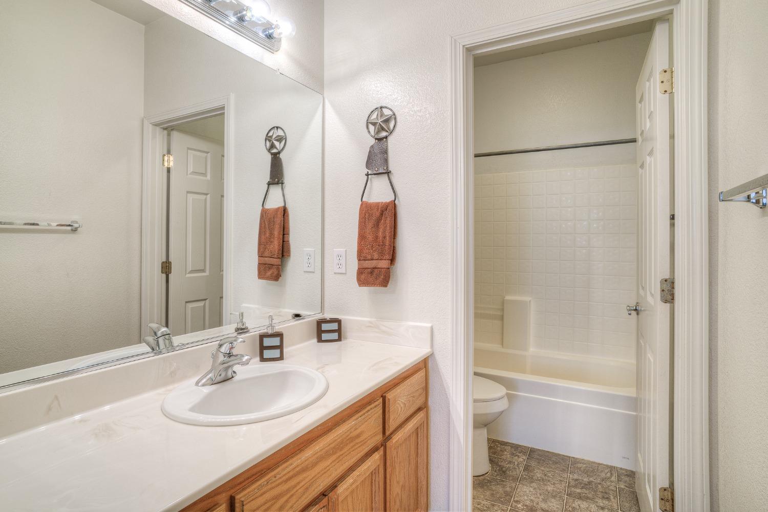 Bathroom with a wood vanity and mirror beside a tiled tub-shower and toilet.
