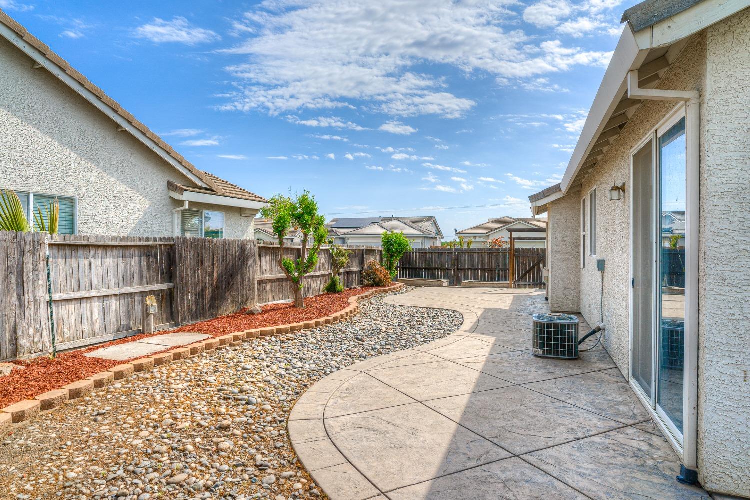 Fenced backyard with a curved stamped-concrete patio, river-rock bed, and mulched planting strip.