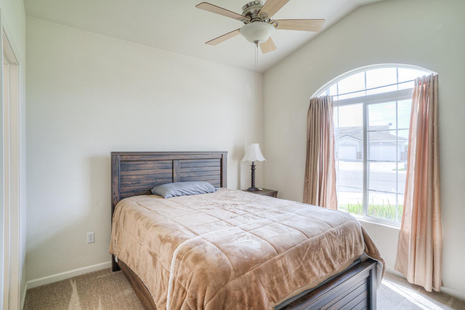 Bedroom with a dark wood bed and large arched window framed by pink curtains.