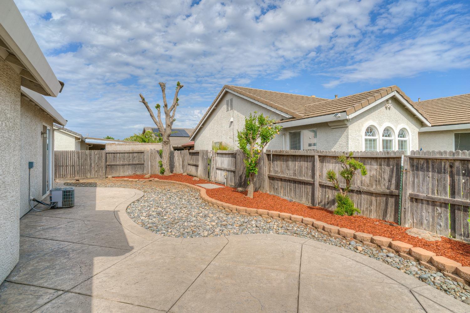 Fenced backyard with a curved concrete patio, decorative rock bed, and three arched house windows.