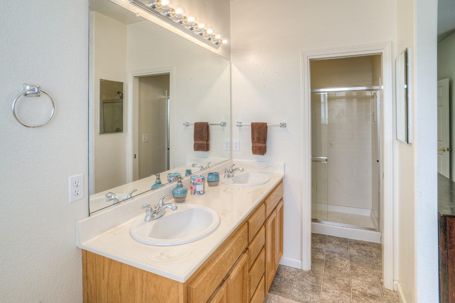 Bathroom with a double-sink vanity, large mirror, wood cabinets, and glass-enclosed shower.