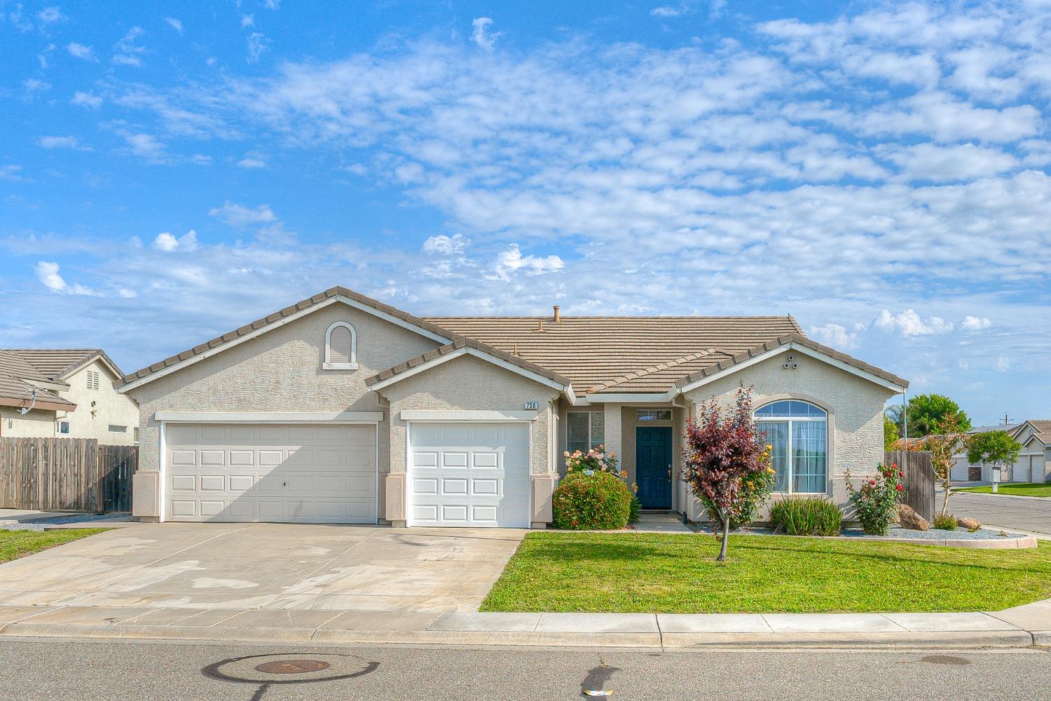 Single-story stucco home with a two-car garage, wide driveway, and flowering front garden.