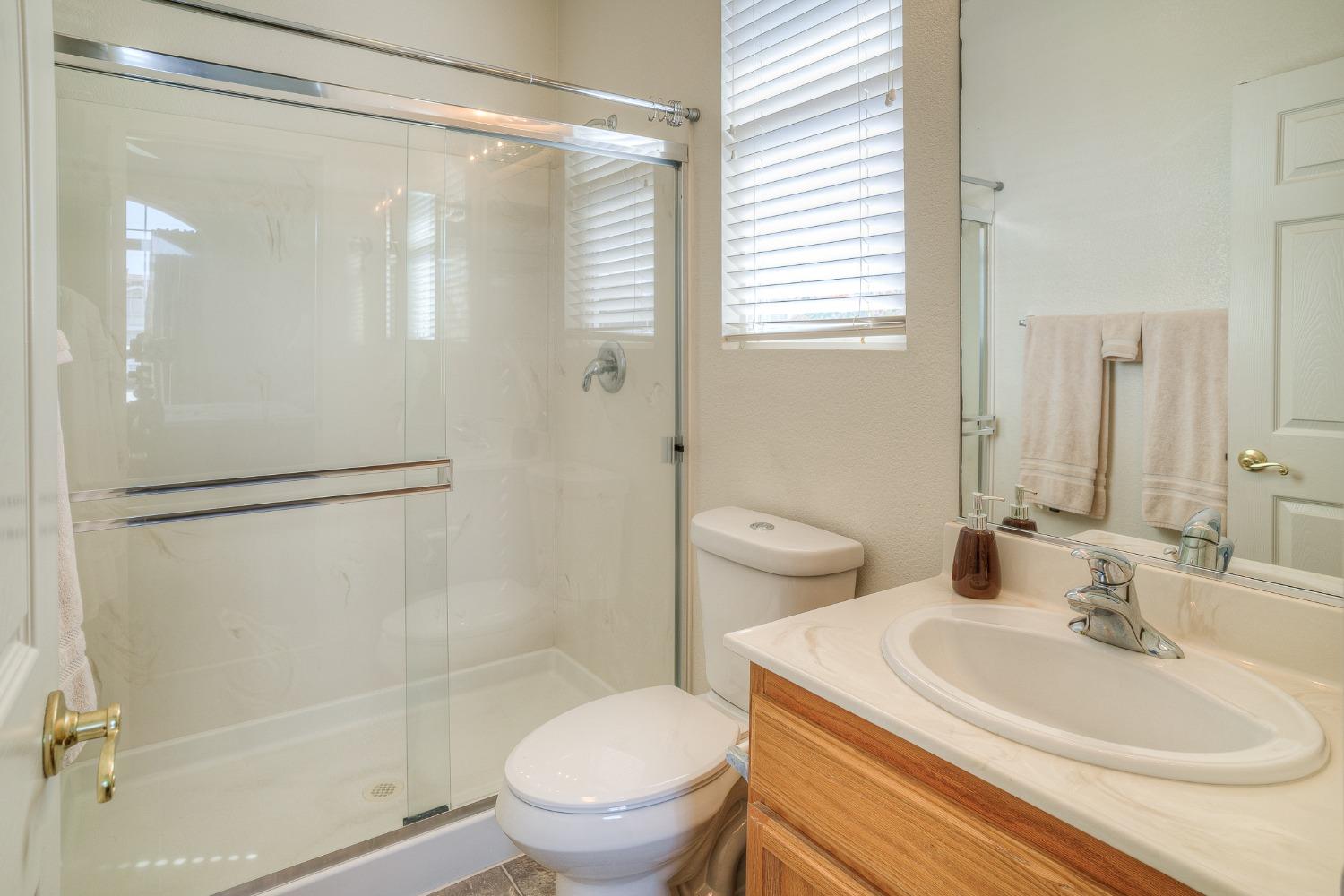 Bathroom with a glass-enclosed shower, wood vanity, and window with blinds.