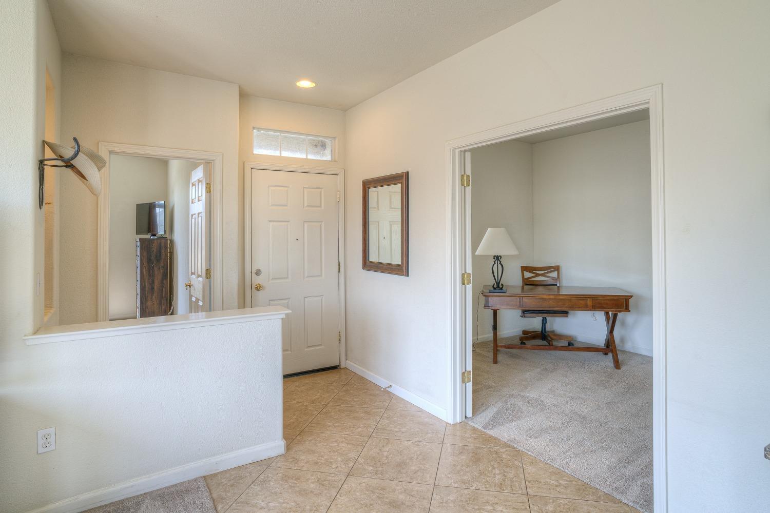 Entry foyer with tiled floors and a front door, opening to a carpeted office with a wooden desk.