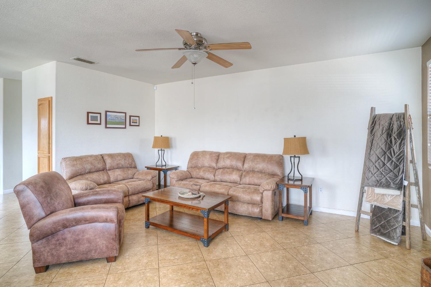 Living room with two sofas, a recliner, a wooden coffee table, and tan tile flooring.