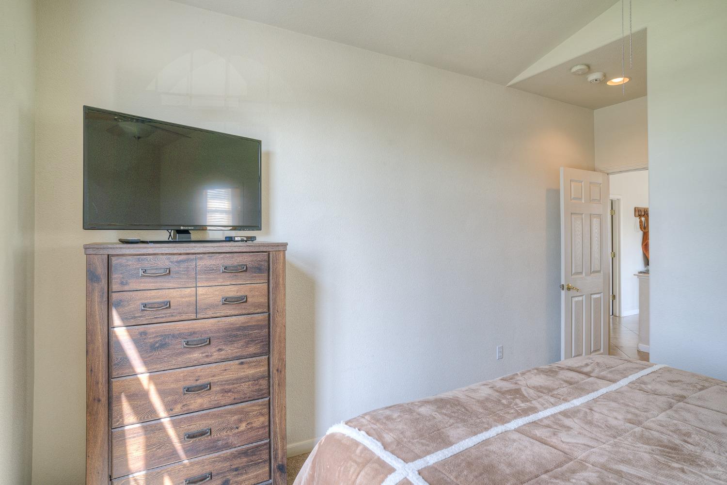 Bedroom with a wooden dresser and television beside a bed under a high, sloped ceiling.