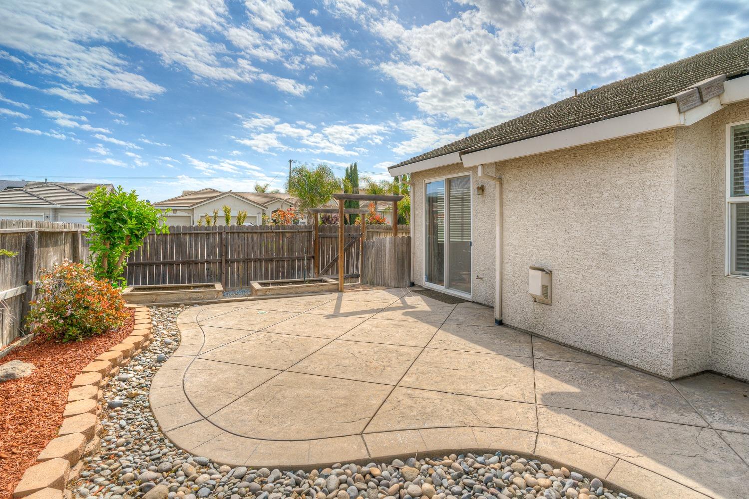 Concrete backyard patio with a small pergola, raised garden beds, and a wooden privacy fence.