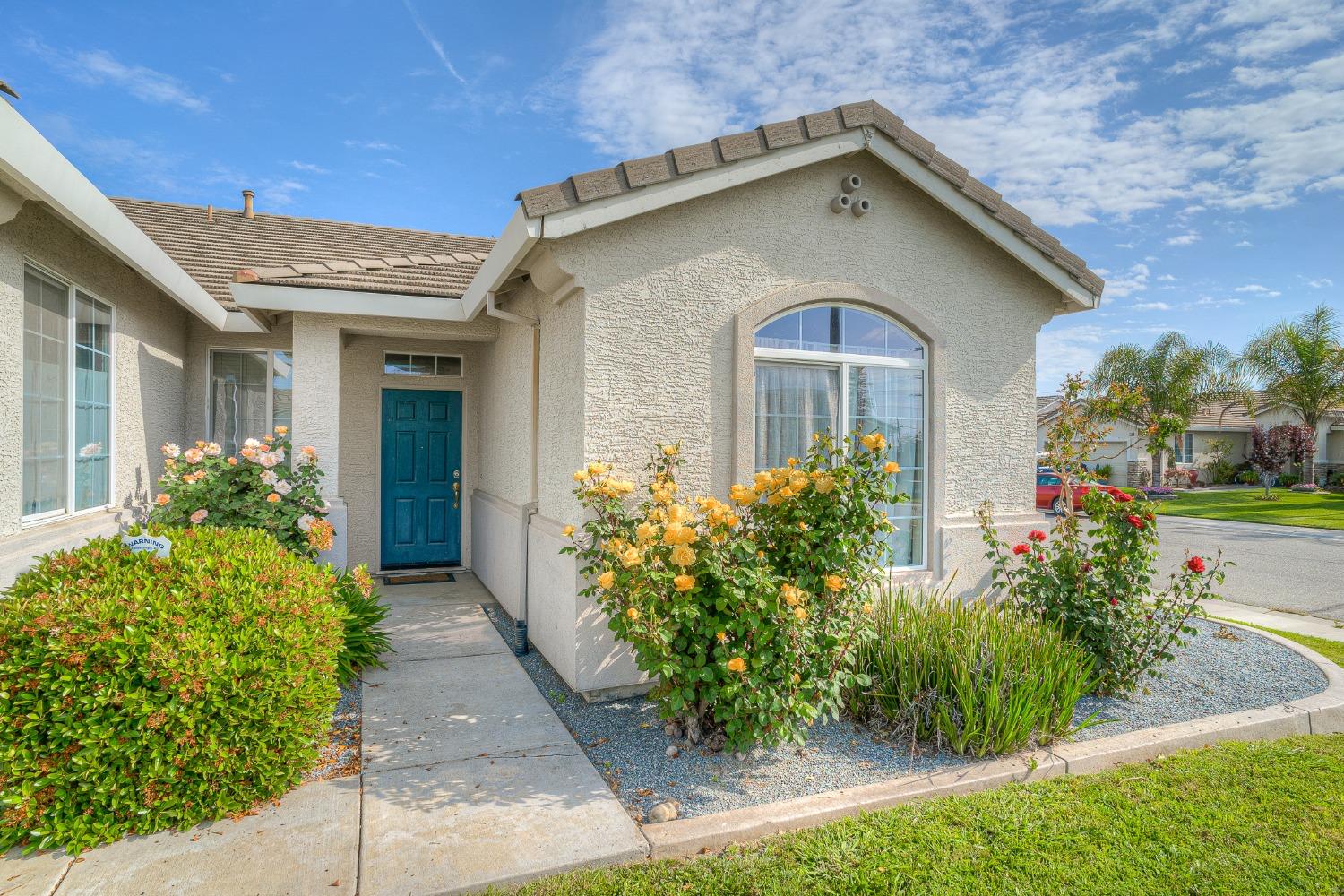 Stucco home with a teal front door, arched window, and flowering rose garden.
