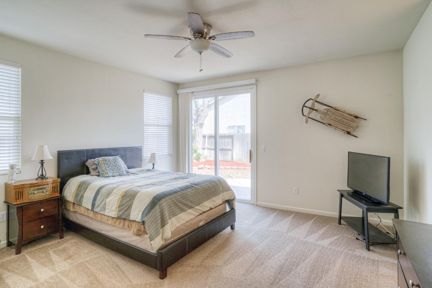 Furnished bedroom with a large bed, sliding glass door, ceiling fan, and television.