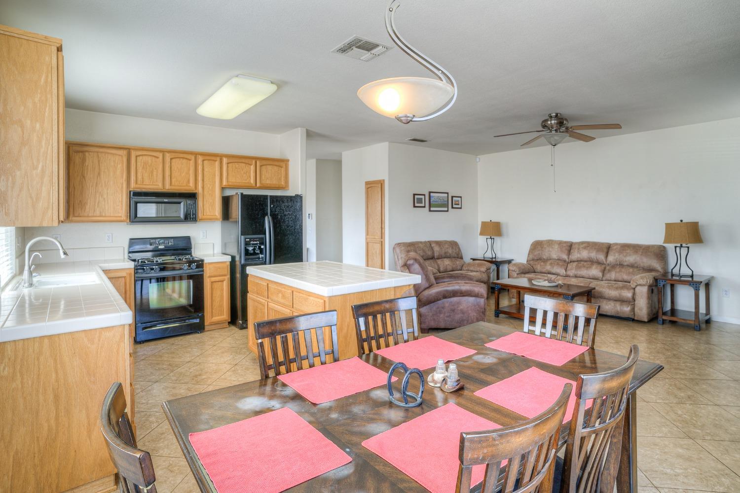 Open-plan kitchen and living room with light wood cabinets, tiled island, and dining table.