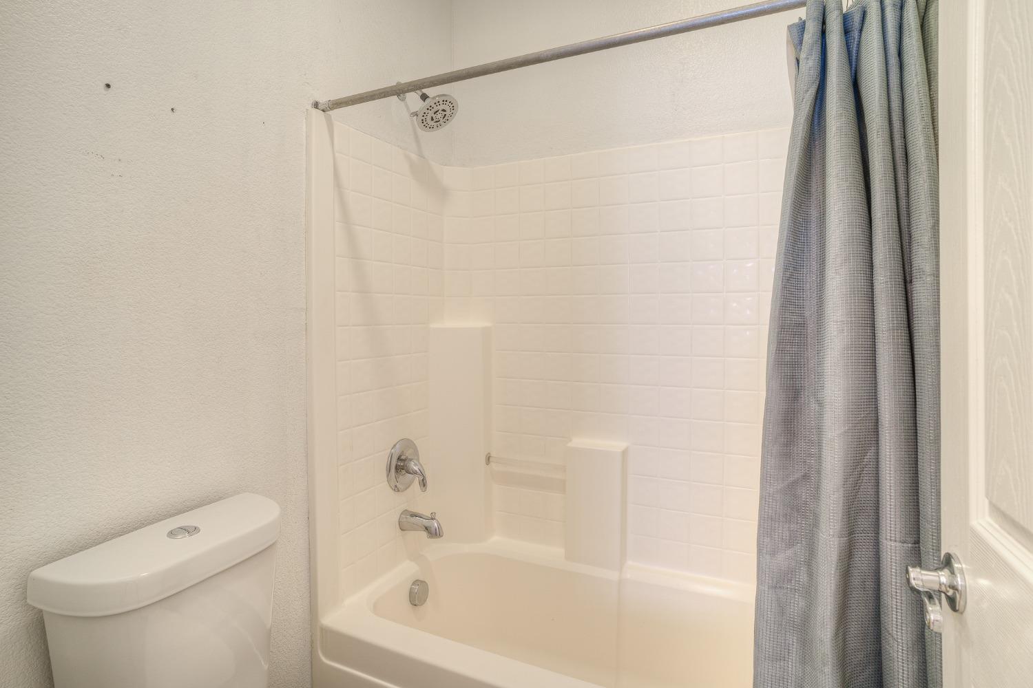 Bathroom with a white tiled tub and shower, gray curtain, and toilet.
