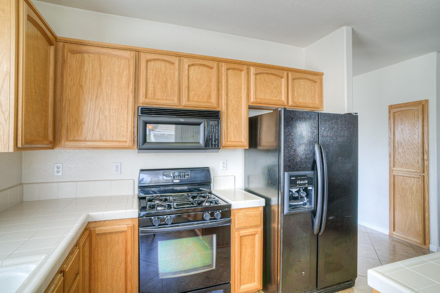 Kitchen with honey-colored cabinets, white tile counters, a black gas range, microwave, and side-by-side refrigerator.