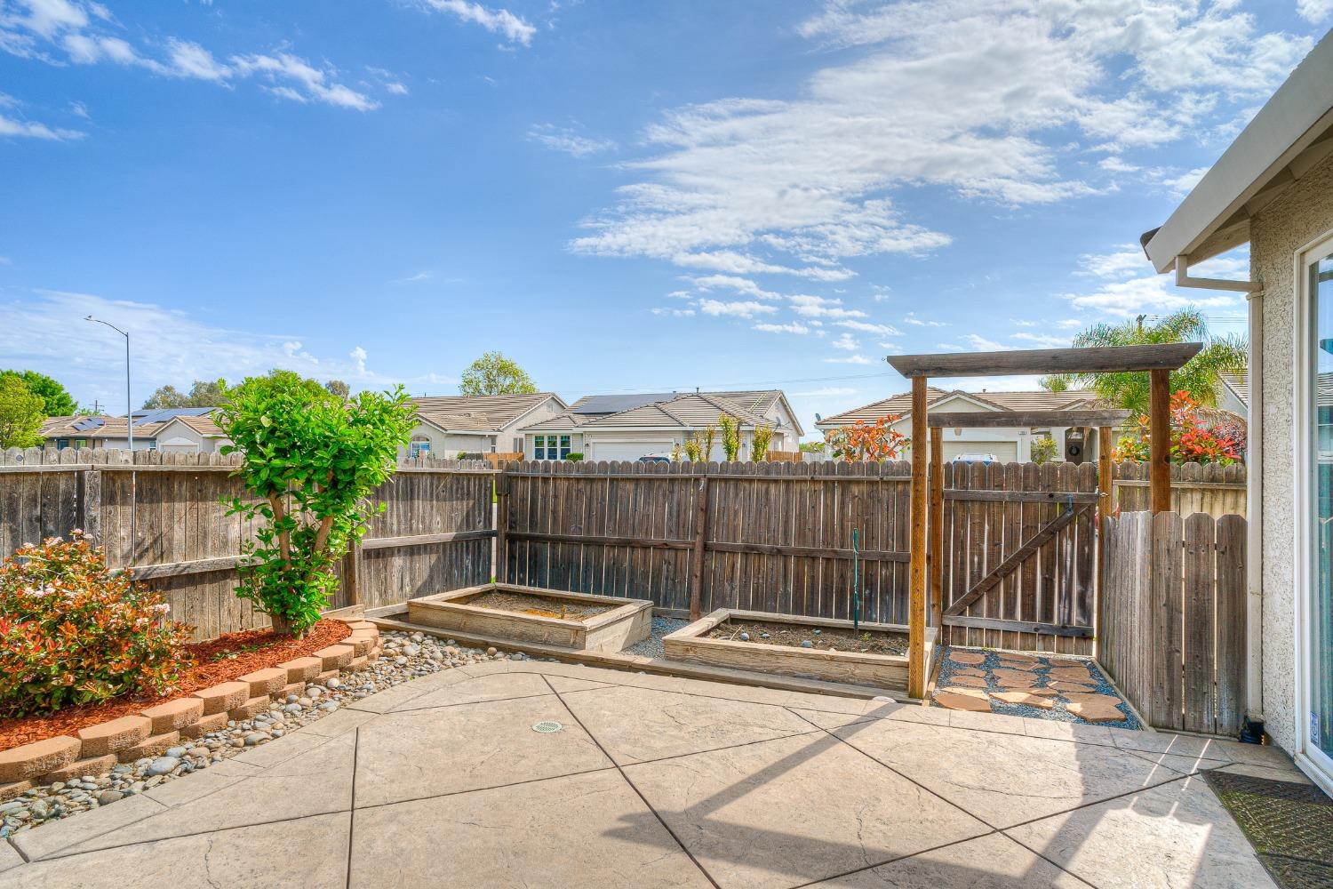 Backyard patio with raised garden beds, a wooden pergola, and a privacy fence.