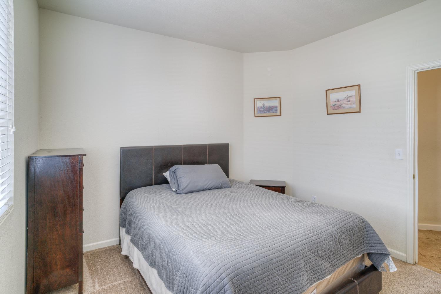 Bedroom with a gray-quilted bed, dark headboard, and wooden cabinet beside a window.