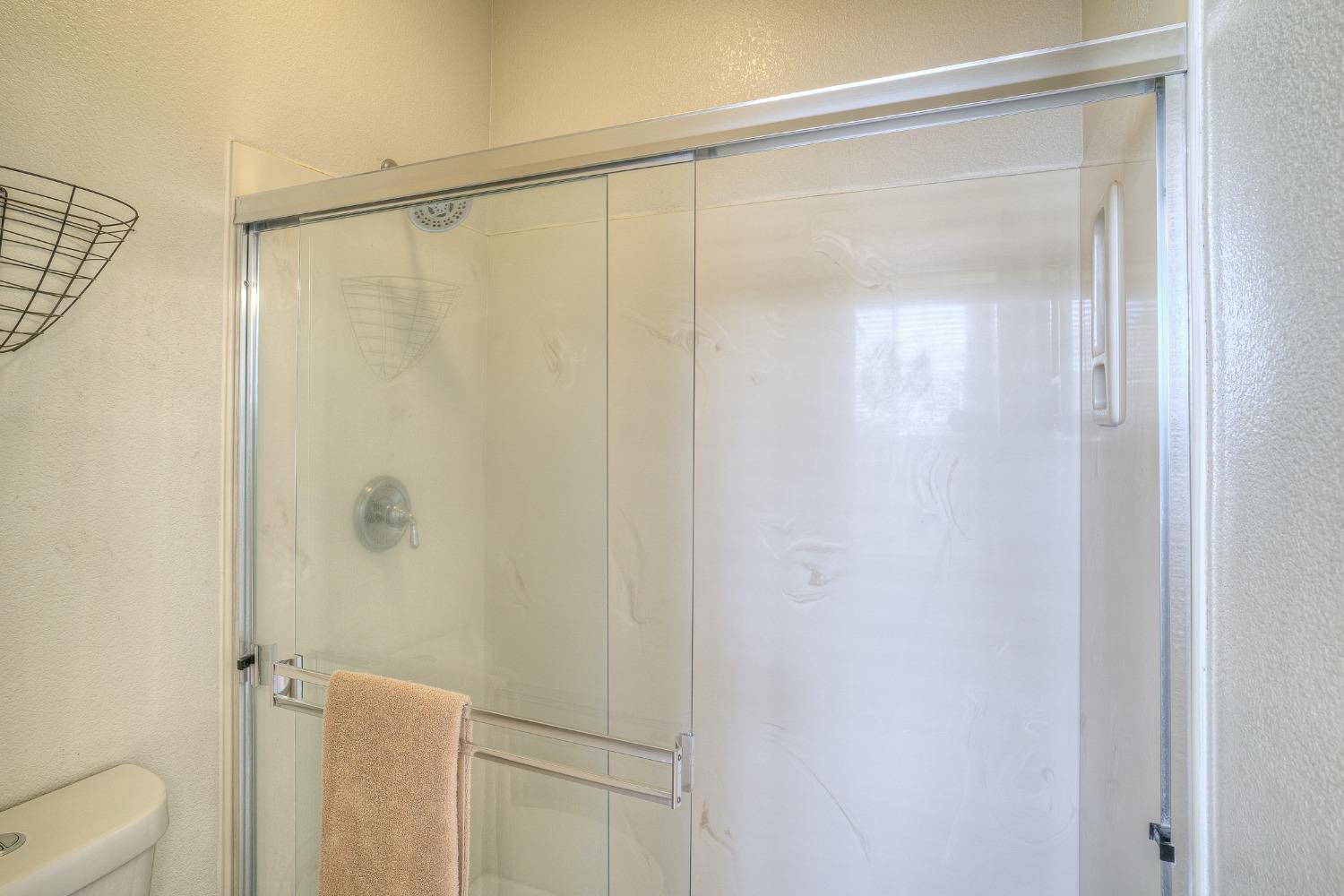 Bathroom shower with sliding glass doors, white surround, chrome fixtures, and a tan towel.