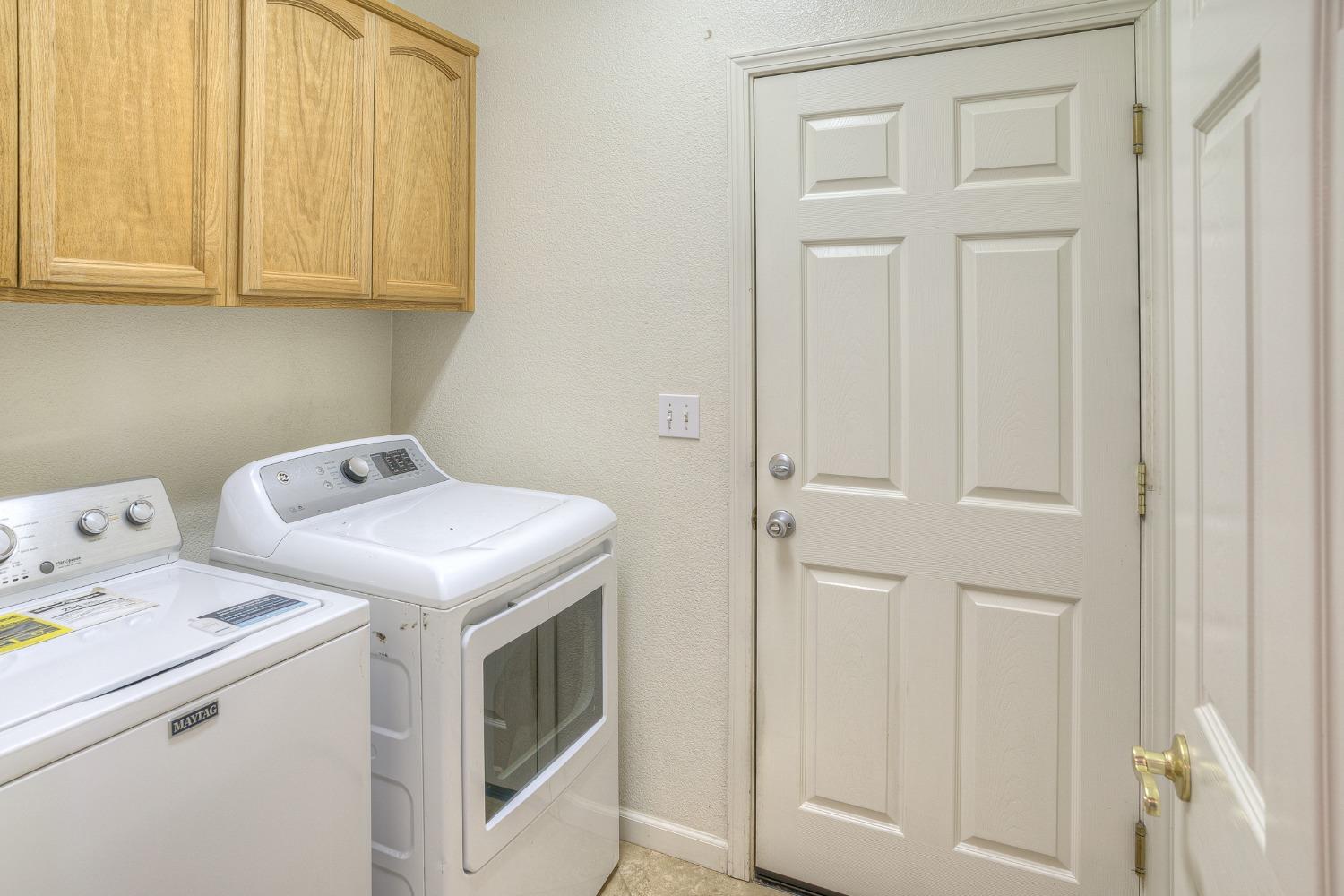 Laundry room with a washer and dryer beneath light wood cabinets, beside a paneled door.