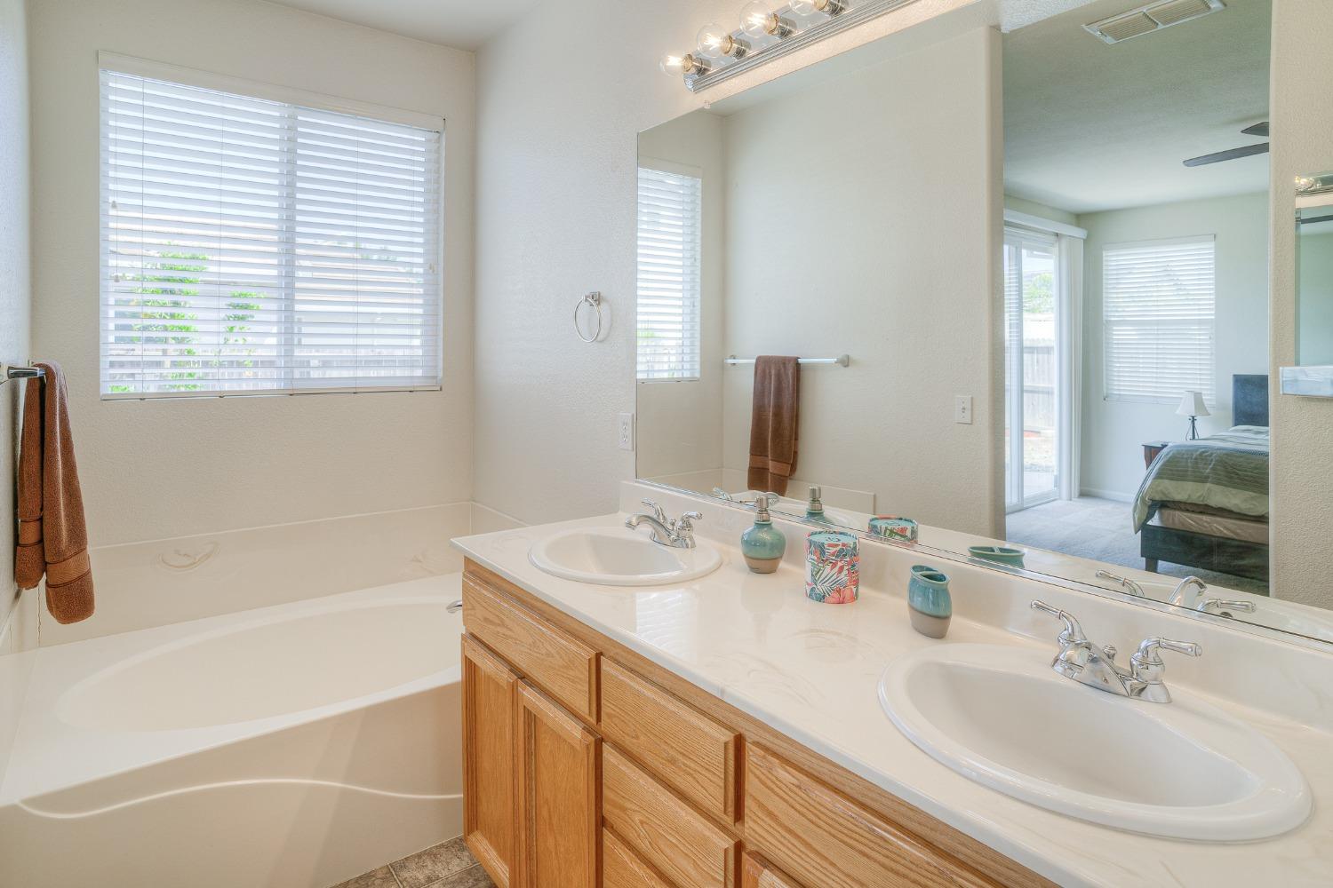 Bathroom with a soaking tub, wide window, and wood double vanity with two sinks.