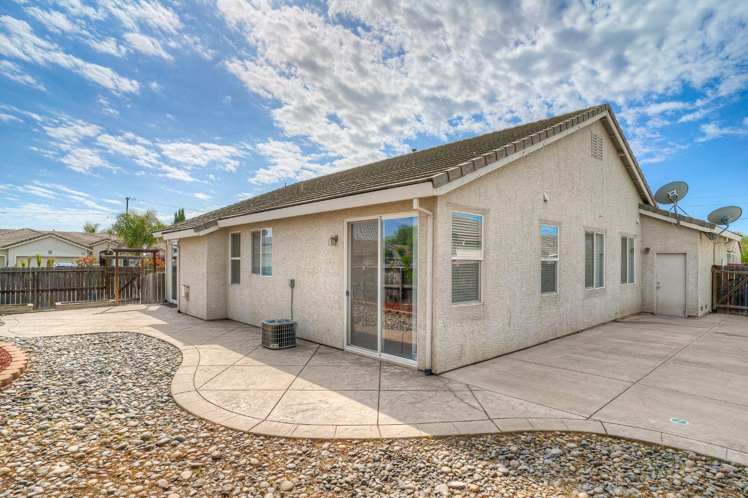 Rear of a single-story stucco home with a sliding door and spacious concrete patio.