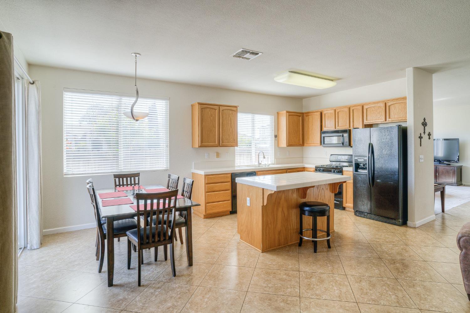 Kitchen and dining area with a central island, wood cabinets, black appliances, and tiled floors.
