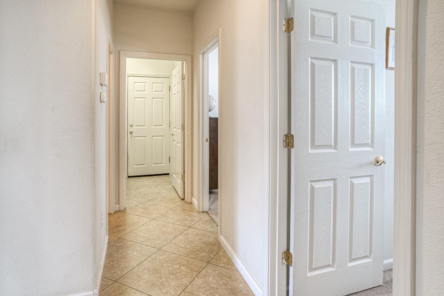 Bright tiled hallway with white paneled doors and an open foreground door.