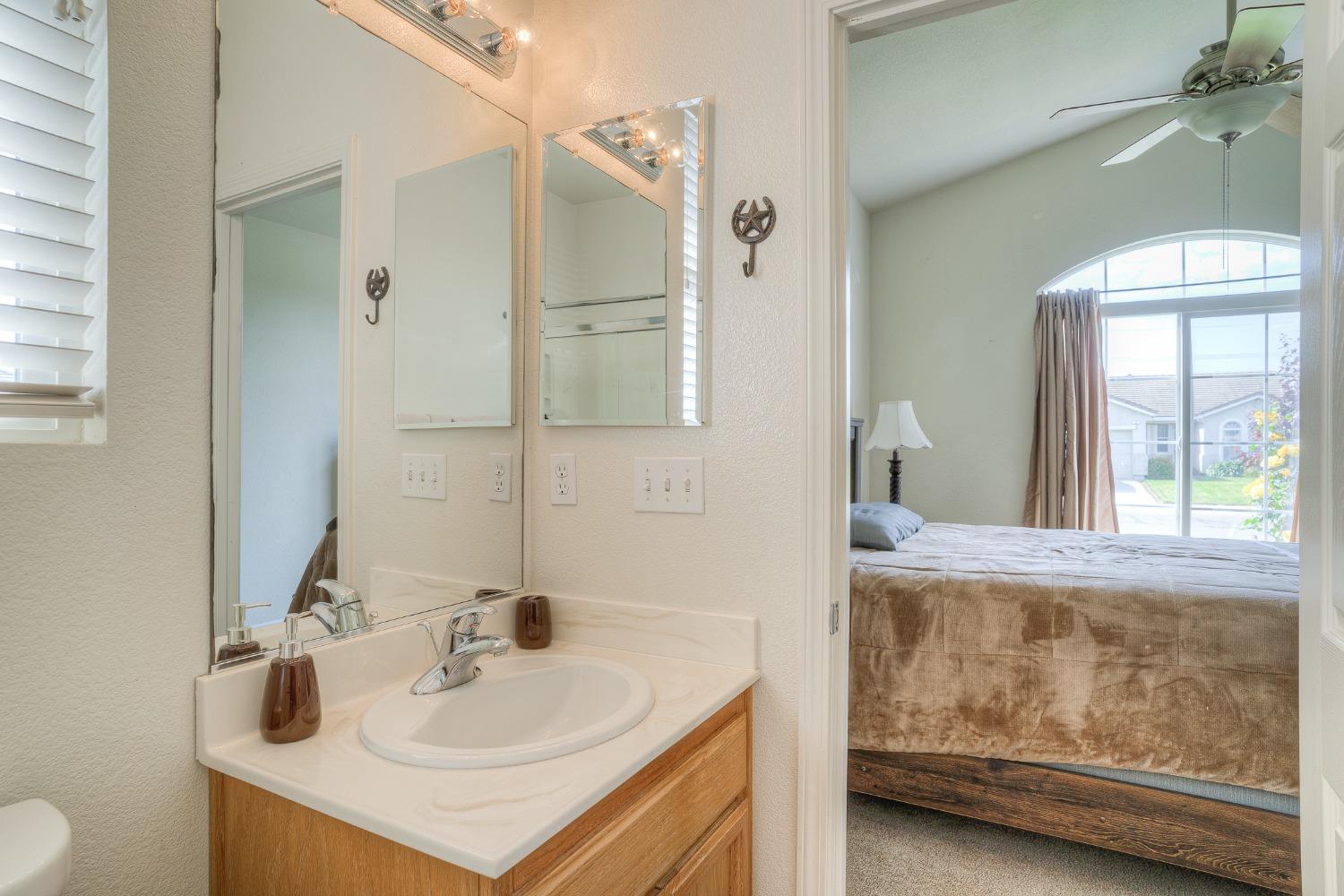 Bathroom vanity with mirrored wall opens onto a bedroom with a large arched window.