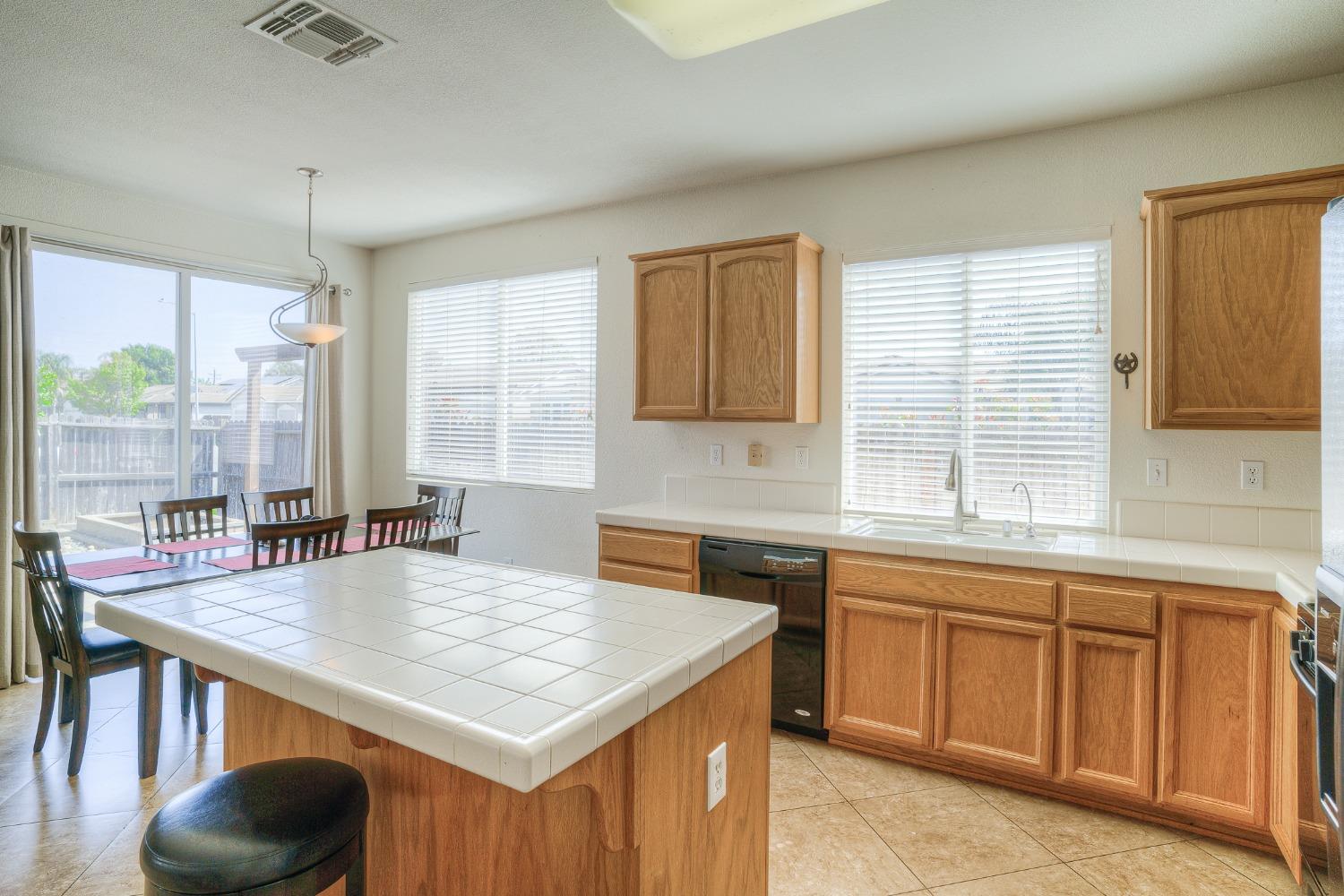 Kitchen with a large tiled island, wood cabinetry, and an adjoining dining area by sliding glass doors.