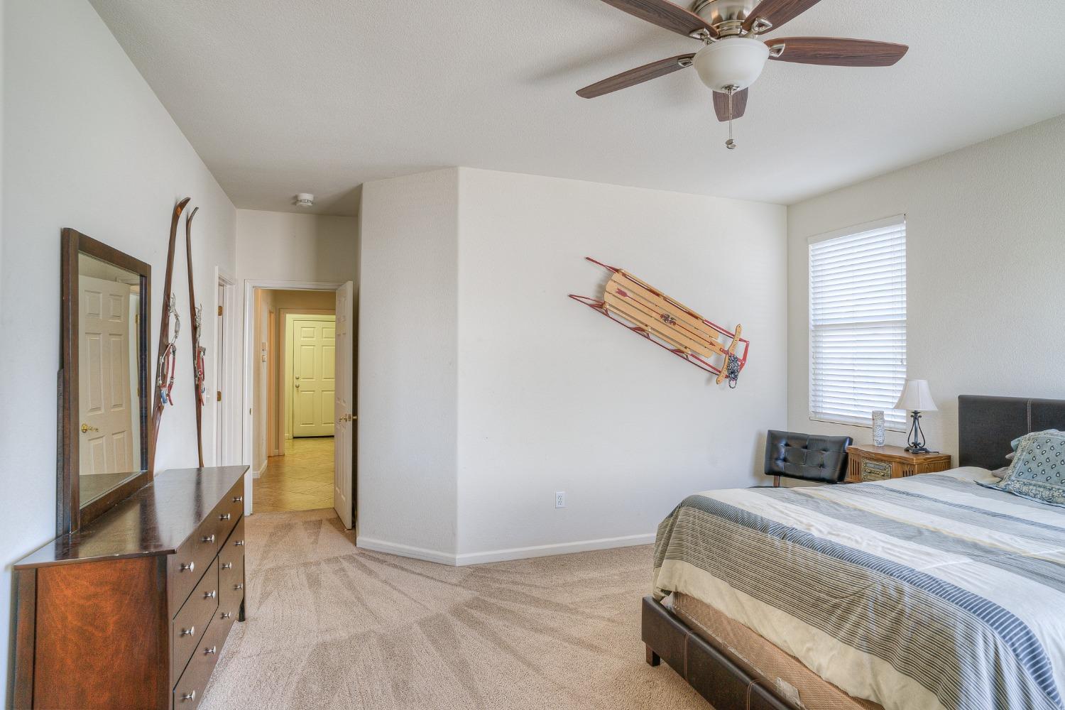 Bedroom with a ceiling fan, beige carpet, and a vintage sled mounted on the wall.