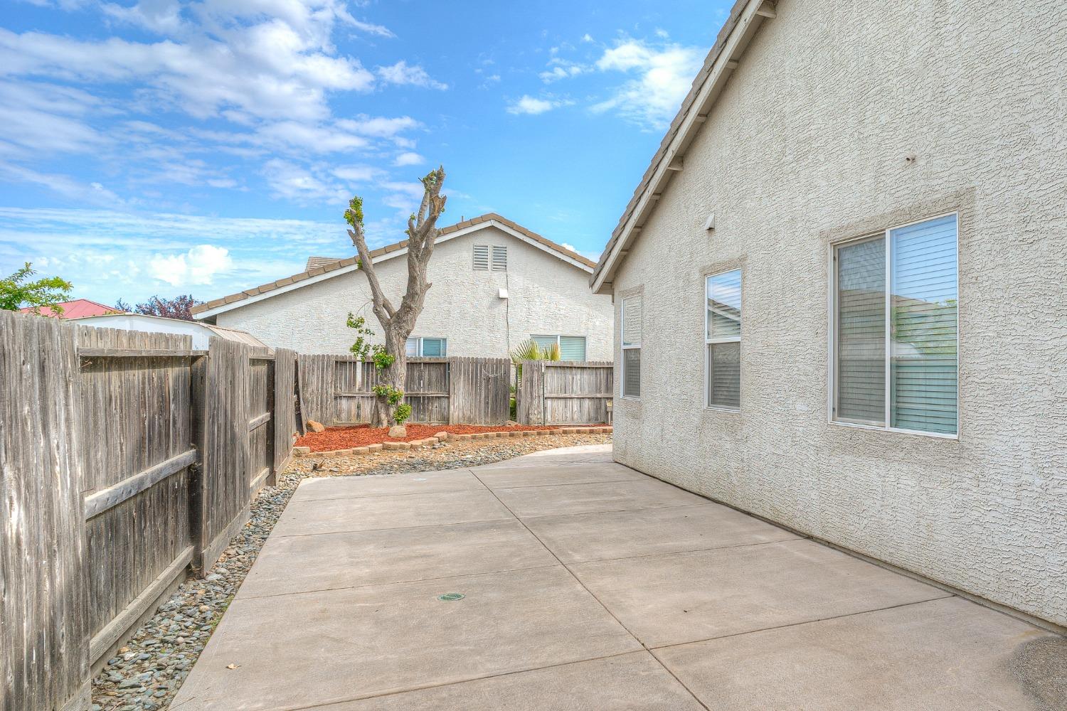 Concrete side patio beside a stucco house, enclosed by a wooden fence and bordered with gravel.
