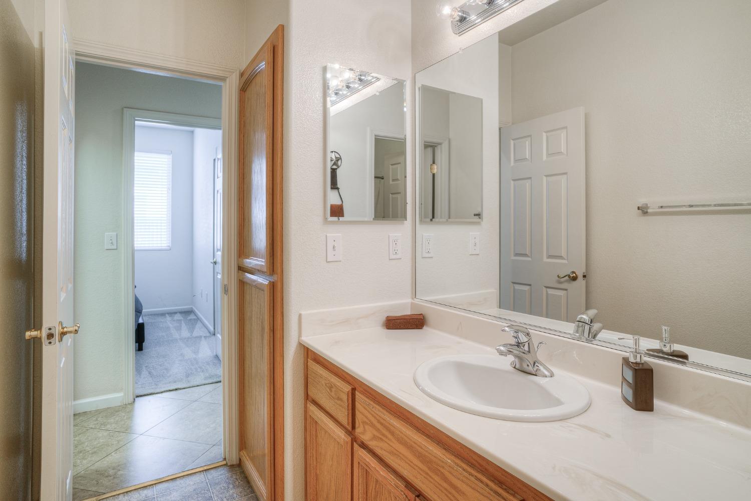 Bathroom vanity with a long white countertop, oval sink, wood cabinets, and large mirrors.