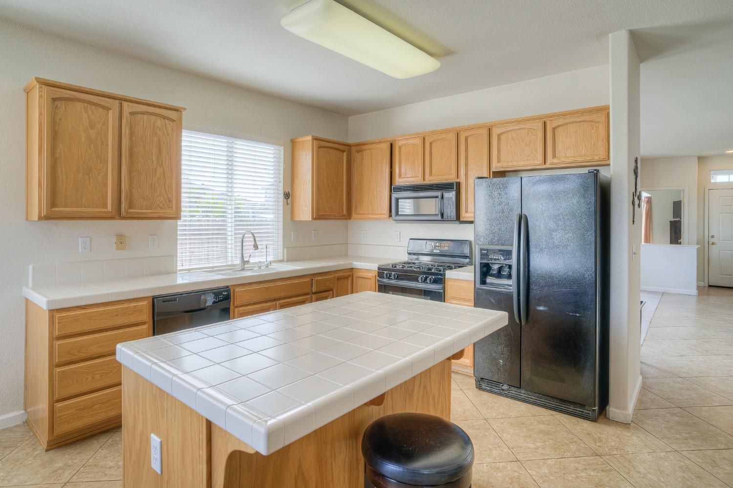 Kitchen with light wood cabinets, a large tiled island, and stainless steel appliances.